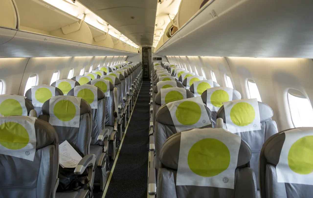 Салон Embraer 170 S7 вдоль прохода: по два кресла с каждой стороны, зелёные круги на подголовниках