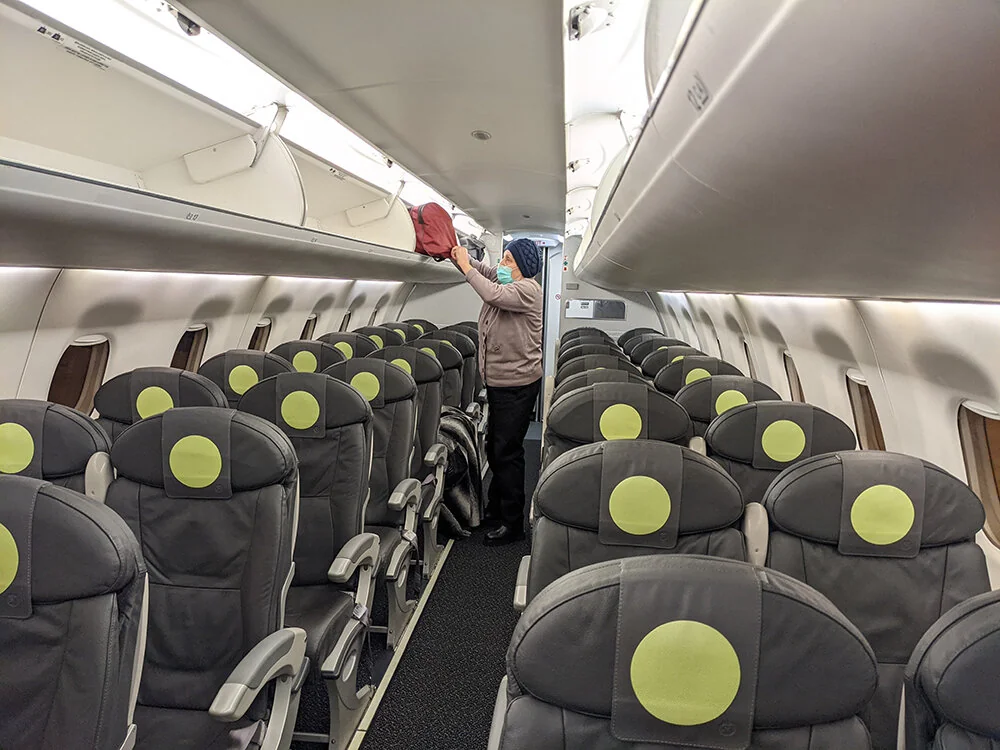 Салон Embraer 170 S7 перед вылетом: пассажир убирает сумку на багажную полку